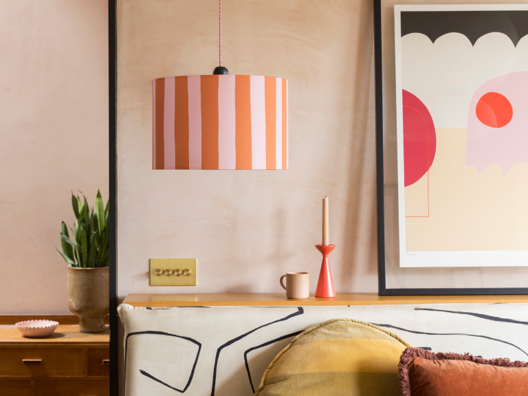 Cotton canvas 35cm drum lampshades with a digitally printed thick, slightly-wobbly vertical orange and pink stripe pattern. The shade is installed as a ceiling light in a bedroom setting.
