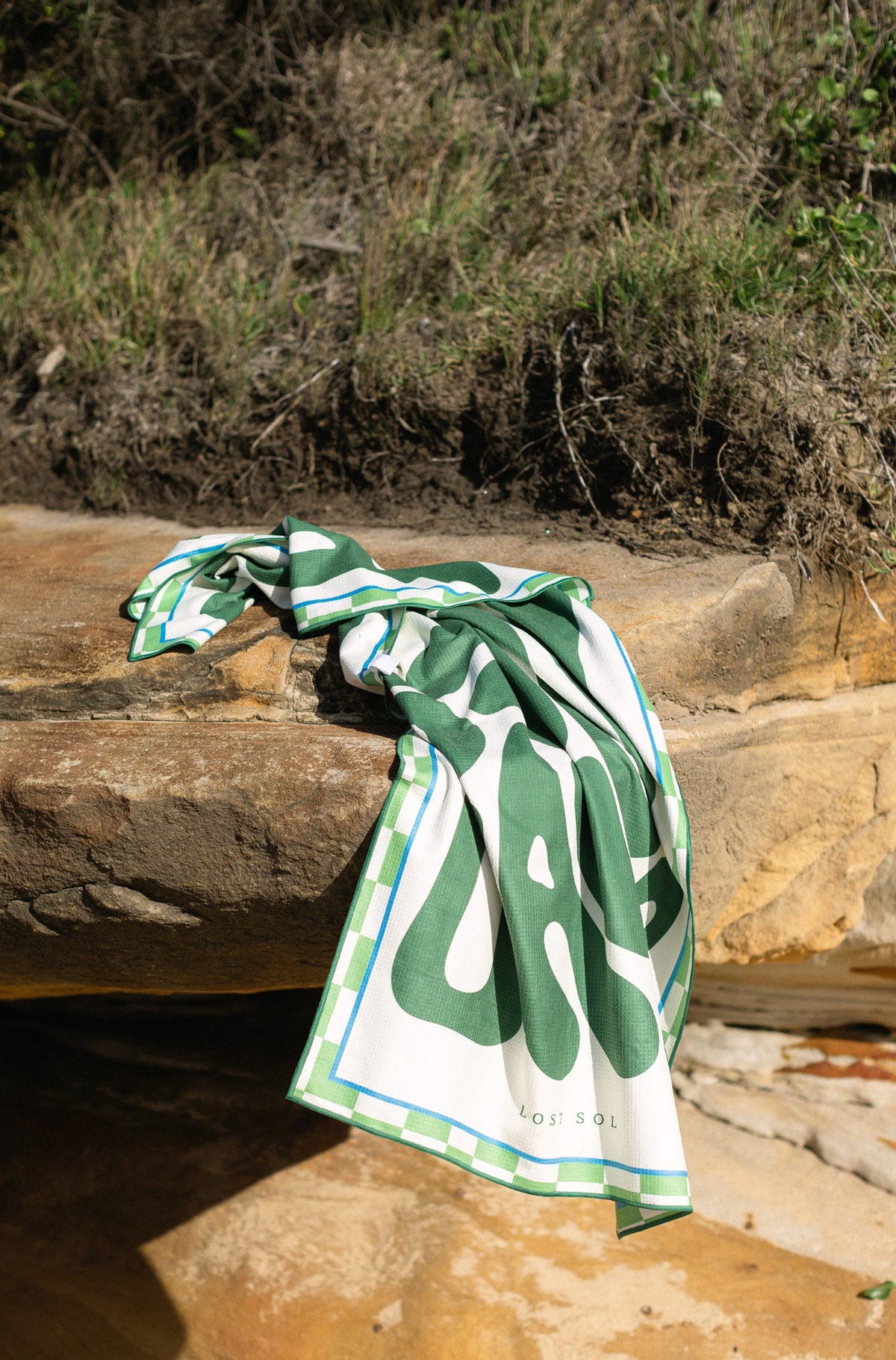 Byron Bay Bold deep green beach towel shaking sand-free on the beach, Lost Sol lifestyle photo