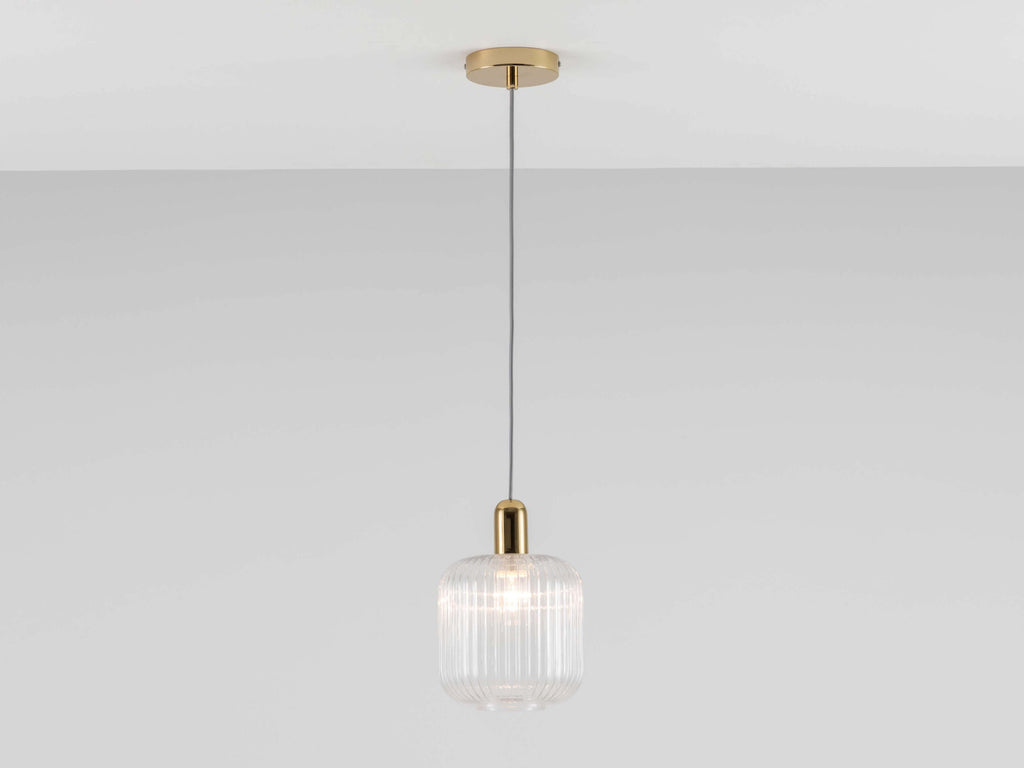 A cube-shaped ribbed glass shade with smooth curved edges is suspended from a ceiling pendant. Light is on.