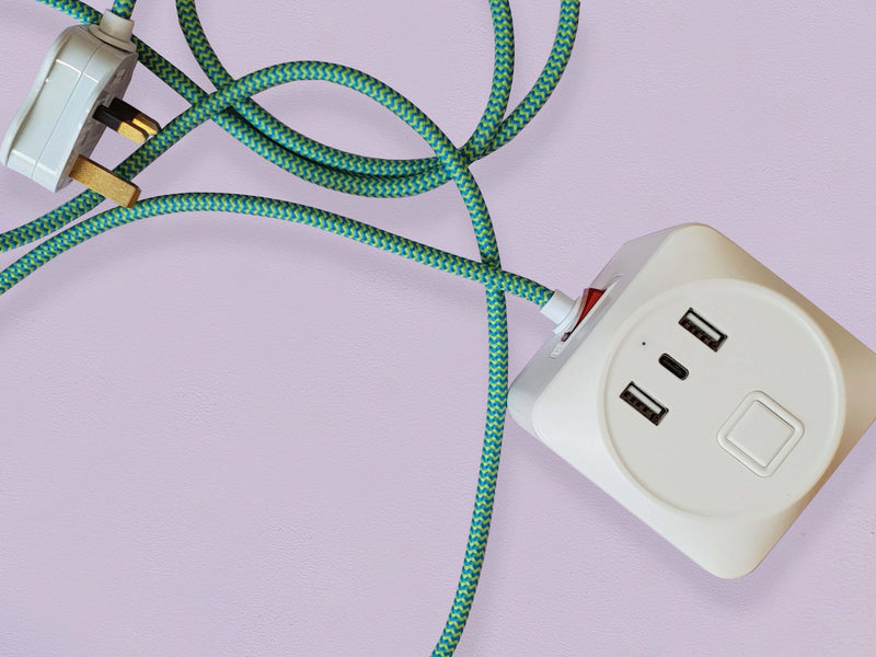 A cuboid extension lead with three plug sockets and three USB sockets, including one USB-C port with green herringbone fabric. Set against a pale lilac background.