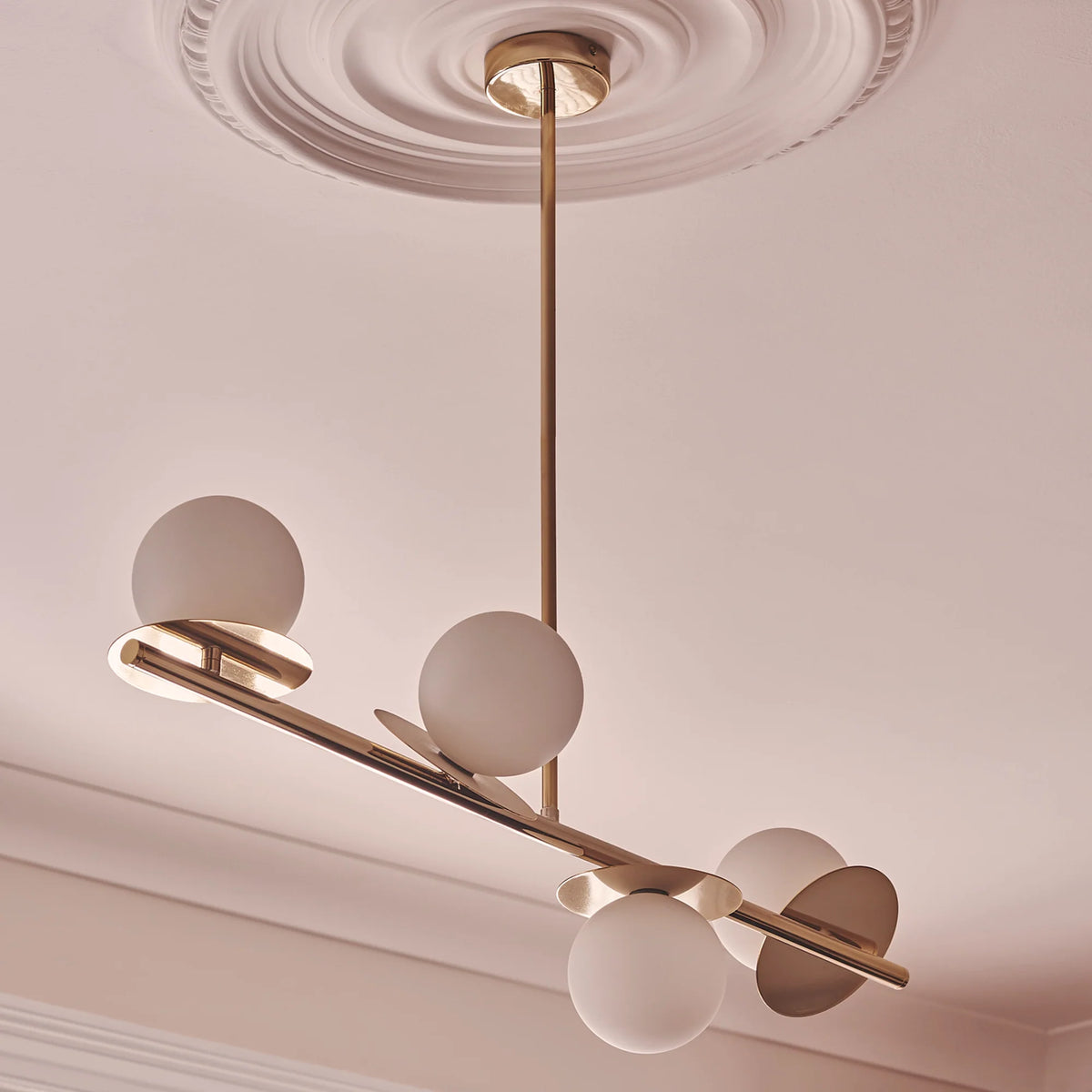 Brass Opal Disk Ceiling Light . A horizontal brass metal stems holds 4 metal disks at varying angles, each topped with an opal glass shade. Light is on.