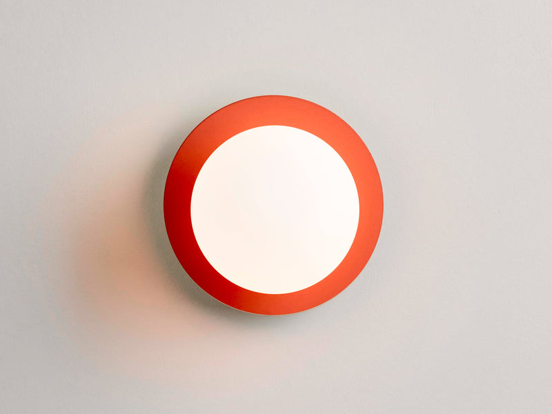 An opal glass shade sits upon an orange metal disk. Light is on. Suitable for bathrooms.