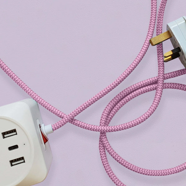 A cuboid extension lead with three plug sockets and three USB sockets, including one USB-C port with pink herringbone fabric. Set against a pale lilac background.