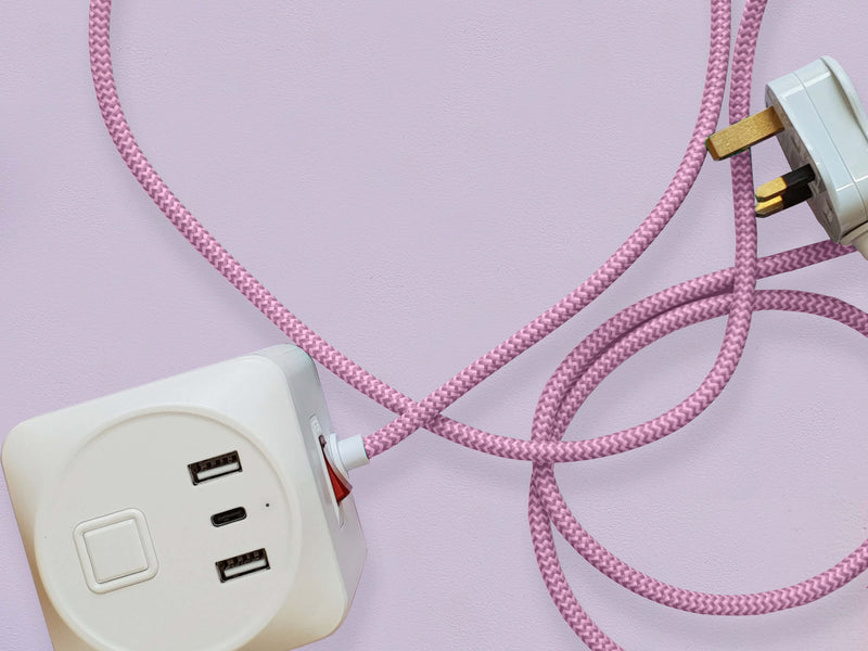 A cuboid extension lead with three plug sockets and three USB sockets, including one USB-C port with pink herringbone fabric. Set against a pale lilac background.