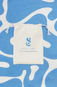 Compact packable Lost Sol Santorini Pastel microfibre towel in soft sky blue, lifestyle photo