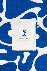 Compact packable Lost Sol Santorini Bold microfibre towel in deep blue and white, lifestyle photo