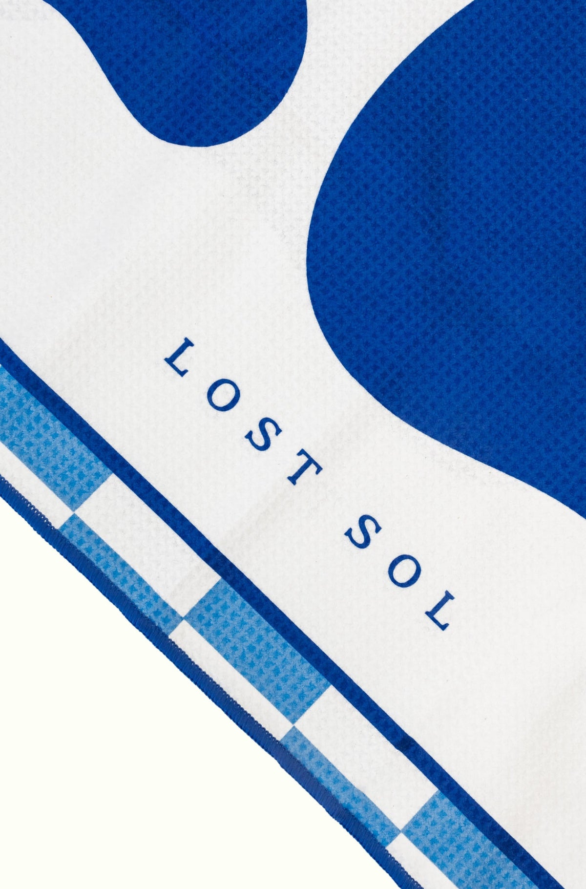 Santorini Bold quick-dry microfibre towel in deep blue and white, folded product shot on a yellow background