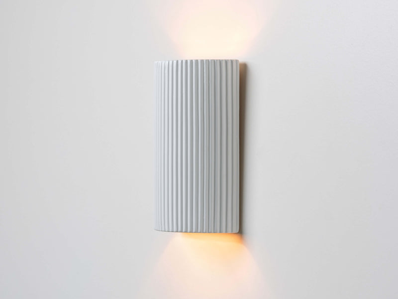 Vertically ribbed ceramic wall light with two bulbs placed either end to create an up-down glow. Lights on.