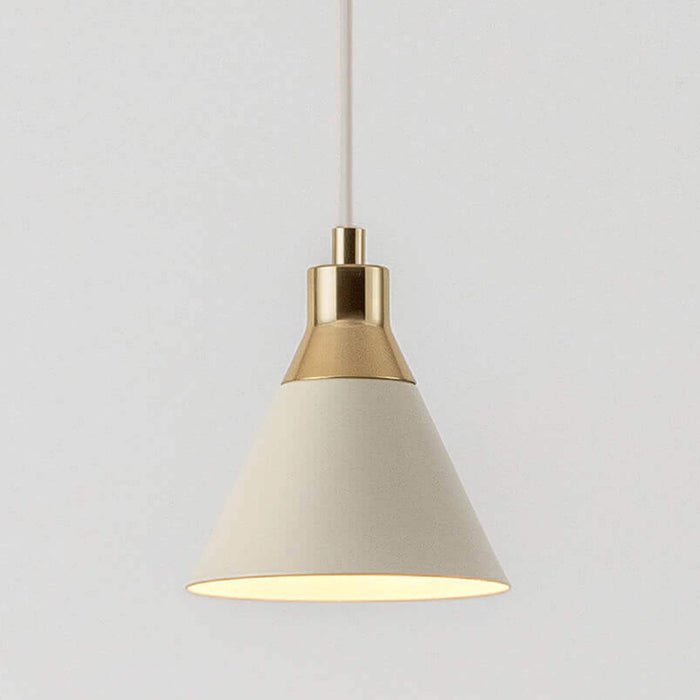 Close up of an adjustable sand ceiling pendant cable suspends a sand metal cone shade with a brass cap. Light is on.