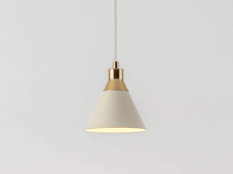 Close up of an adjustable sand ceiling pendant cable suspends a sand metal cone shade with a brass cap. Light is on.