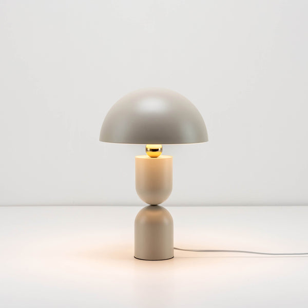 A sand-coloured metal dome containing integrated LED bulbs forms the top of the mushroom-shaped table lamp with brass sphere detail where the base and head meet. Light is on.