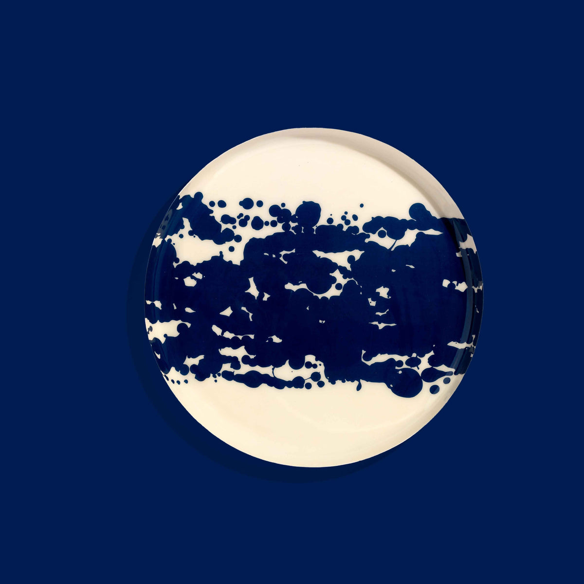 Zero round enamel tray in cream with a large abstract dark blue splash by Geese