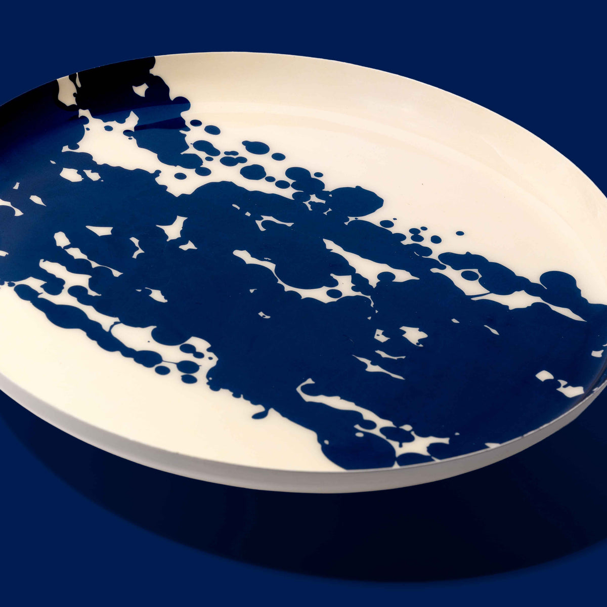 Zero round enamel tray in cream with a large abstract dark blue splash by Geese