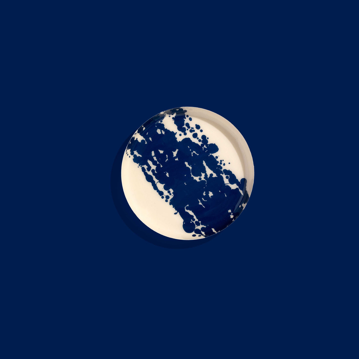 Zero round enamel tray in cream with a large abstract dark blue splash by Geese
