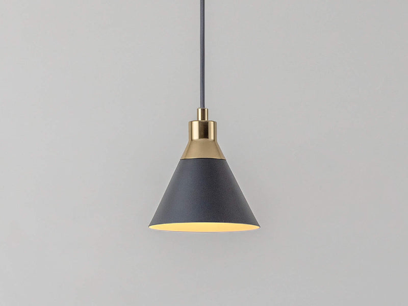 An adjustable grey ceiling pendant cable suspends a charcoal-grey metal cone shade with a brass cap. Light is on.