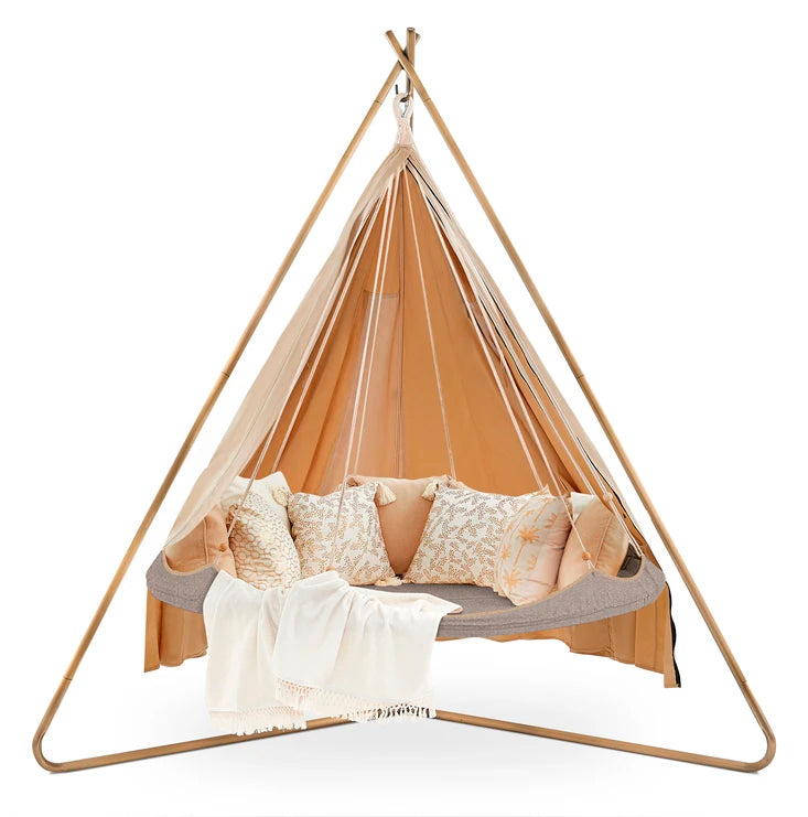 Bohemian-style hanging bed with a beige canopy, pillows, and a throw blanket, suitable for outdoor relaxation.